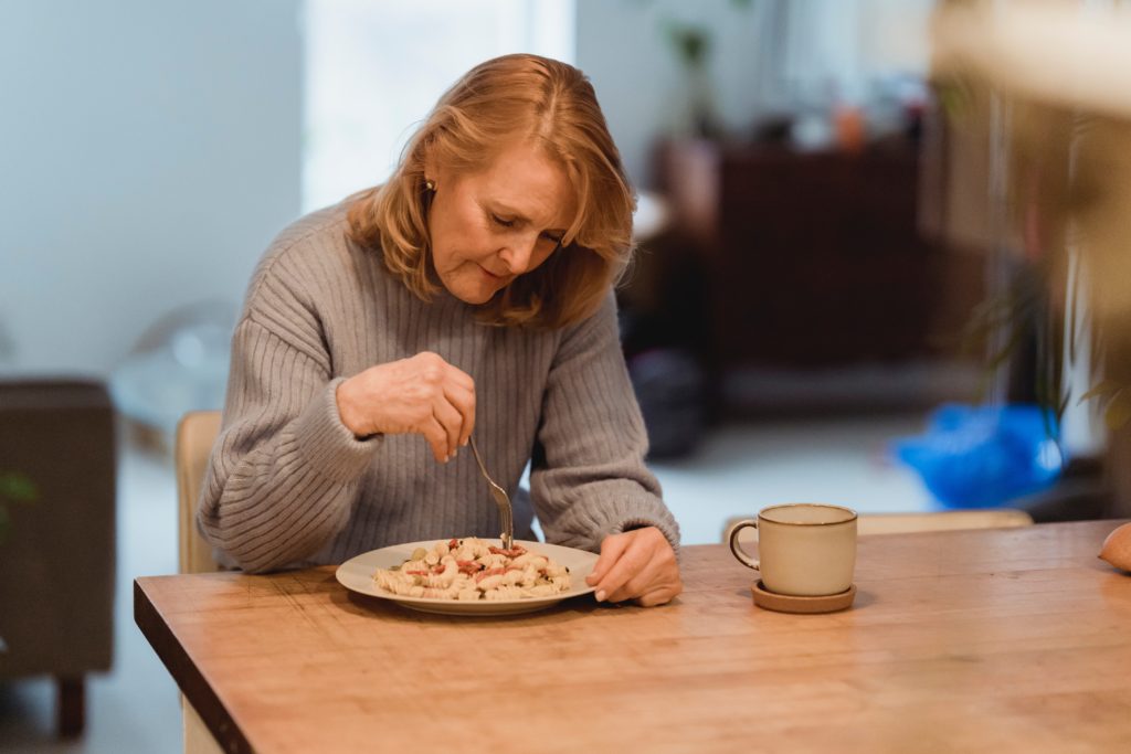 A woman sitting at a table alone eating unhealthy food. but should focus on keto for women over 50.